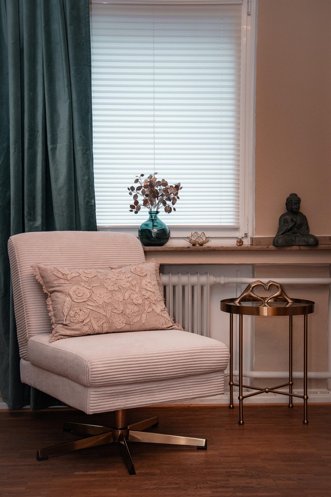 Ein Sessel mit Kissen am Fenster, daneben ein kleiner goldener Beistelltisch